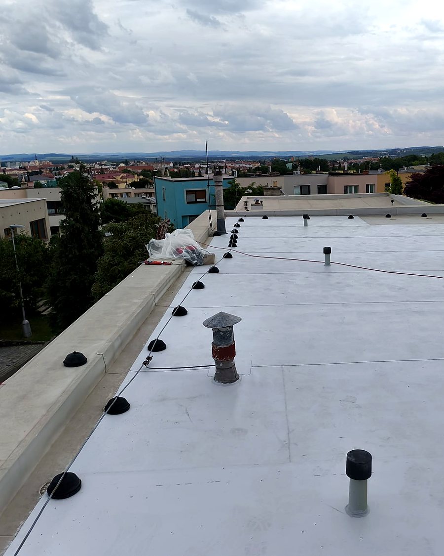 Plochá střecha s novou světlou PVC fólií, za atikou výhled na město