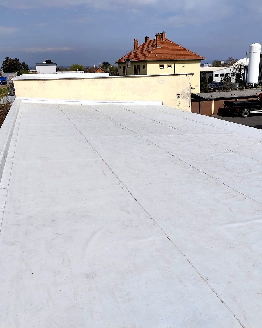 Plochá střecha se světlou fólií, v pozadí domy